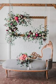 a couch with flowers and greenery hanging from it's back, in front of a white brick wall