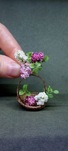 a miniature basket with flowers in it being held by a person's hand on a gray surface