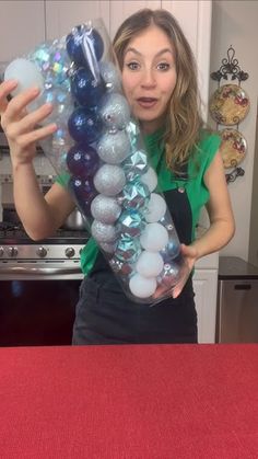 a woman is holding up some ornaments in her hand while standing at the kitchen counter