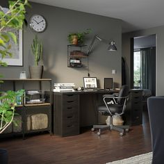 an office with a desk, chair and clock on the wall next to a potted plant