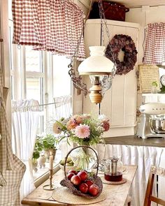 a wooden table topped with a basket filled with fruit next to a window covered in checkered curtains