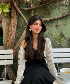 a woman sitting on a white bench next to a cup of coffee