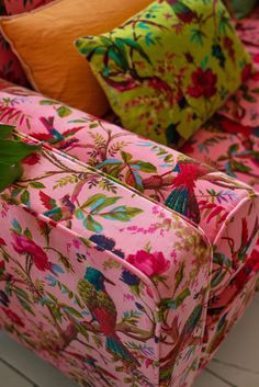 a pink floral couch sitting on top of a white wooden floor next to green plants