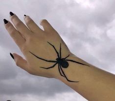 a woman's hand with a black spider tattoo on her wrist and the sky in the background