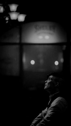 black and white photograph of a man sitting in front of a subway train at night