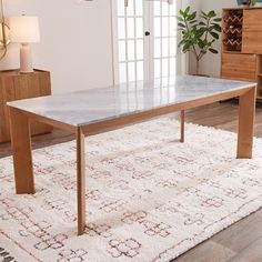 a marble top dining table on a rug in front of a wooden cabinet and dresser