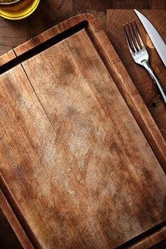 a wooden cutting board sitting on top of a table next to a knife and fork