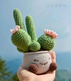 a hand holding a small crocheted cactus in a pot with flowers on it