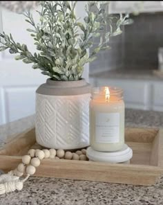 a candle sits on a tray next to a plant and some beads in front of it