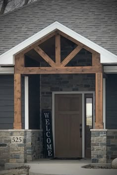 a welcome sign in front of a house with stone pillars and wood framed entryway