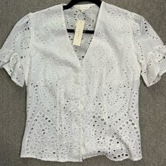 a white blouse with an openwork design on the front and back, hanging on a hanger