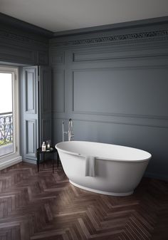 a large white bath tub sitting on top of a wooden floor next to a window