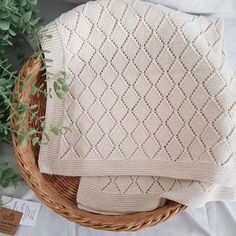 two knitted blankets sitting on top of a basket next to a potted plant