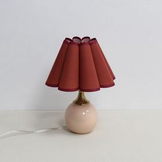 a lamp that is sitting on top of a white table with a red lampshade