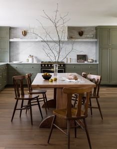 a kitchen with green cabinets and wooden chairs around a table in front of an oven