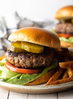 a hamburger with lettuce, pickles and tomatoes on a plate next to french fries