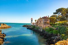 an old house sitting on top of a cliff next to the ocean with a lighthouse in the background