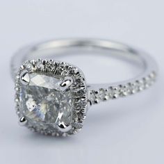 an engagement ring with a cushion - cut diamond surrounded by pave set round diamonds