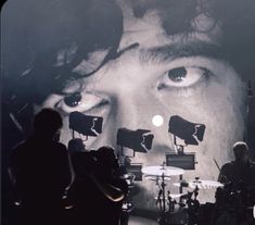 the band is performing on stage in front of a large screen with an image of a man's face