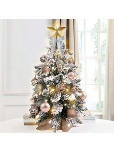 a white christmas tree with gold and silver ornaments on it's base, in front of a window