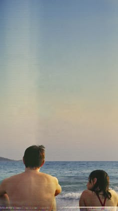 two people sitting on the beach looking out at the ocean