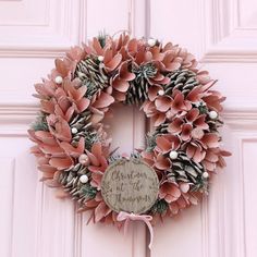 a wreath with pine cones and berries hanging from the front door, on a pink door