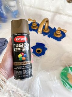 a person holding a spray can in front of a sink with gold faucets