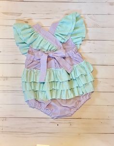 "Perfect for a \"sweet one\" ice cream themed birthday! With ruffled shoulders and ruffles on the bottom, this is the most darling little sunsuit ever! Made of a pretty lilac seersucker with soft mint green seersucker ruffles, it is cool and sweet for a summer party. Available with numbers 1-4. Choose from ruffled shoulder straps that tie in the back with a bow, or that button at the waistband. Shoulders straps can have no ruffles, a single layer of ruffles, or a double layer of ruffles. The bac Flutter Sleeve Bubble Romper With Ruffles For Playtime, Short Sleeve Bubble Romper For First Birthday In Summer, Summer Short Sleeve Bubble Romper For First Birthday, Summer Bubble Romper With Ruffles For Beach, Spring Cute Bubble Romper With Ruffle Sleeves, Cute Bubble Romper With Ruffles And Short Sleeves, Cute Short Sleeve Bubble Romper With Ruffles, Pink Ruffles Bubble Romper For Cake Smash, Playful Ruffle Bubble Romper For Playdate