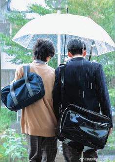 two people walking in the rain with an umbrella over their heads and backpacks under them