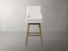 an upholstered bar stool with wooden legs in front of a plain wall and concrete floor