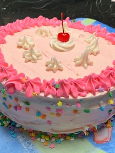 a birthday cake with pink frosting and sprinkles on it, topped with a cherry