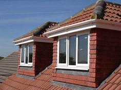 two windows on the roof of a red brick building with white trim and shingles