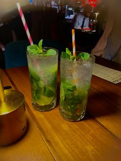 two glasses filled with green drinks sitting on top of a wooden table next to each other