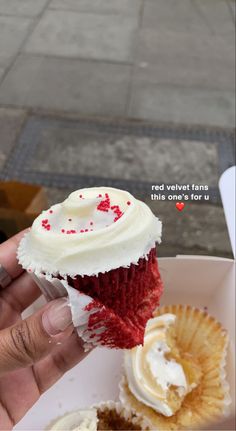 a hand holding a cupcake with white frosting and red sprinkles