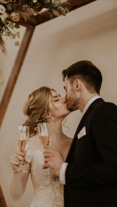 a bride and groom kissing while holding champagne flutes