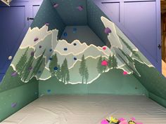 an indoor climbing wall with mountains and trees painted on it