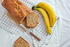 a loaf of banana bread sitting on top of a table next to two bananas and a knife