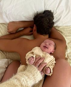 a man is holding a baby while laying on a bed with a white dog next to him