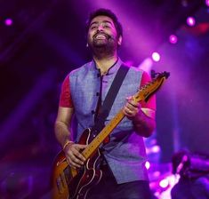 a man that is standing up with a guitar in his hand and smiling at the camera