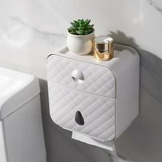 a white toilet paper holder with a potted plant on top