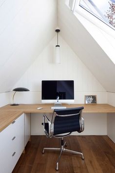 a desk with a computer on top of it in a room under a slanted roof