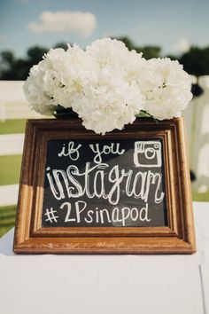 a chalkboard sign with white flowers in it sitting on top of a wooden table