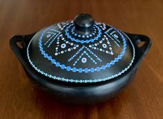 a black pot with blue and white designs on it sitting on a wooden table top