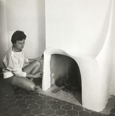 a man sitting on the floor in front of a small white fire place with his legs crossed