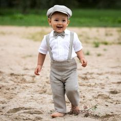 a little boy that is standing in the sand with a bow tie and suspenders