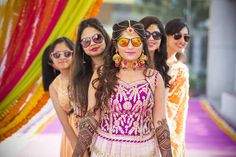 a group of women standing next to each other in front of a colorful curtain and wearing sun glasses