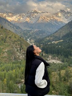 a woman looking up into the sky with mountains in the background