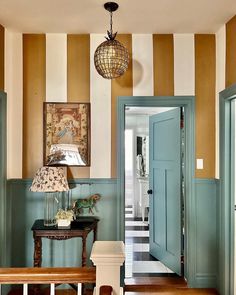 an entryway with striped walls and wooden flooring, blue front door leading to the hallway