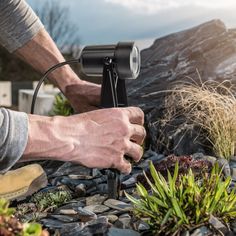 a man using a garden light to plant some plants in the rocks and grass on the ground