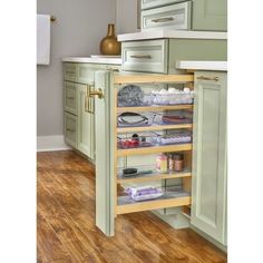 an open cabinet in the middle of a kitchen with wooden floors and green cupboards